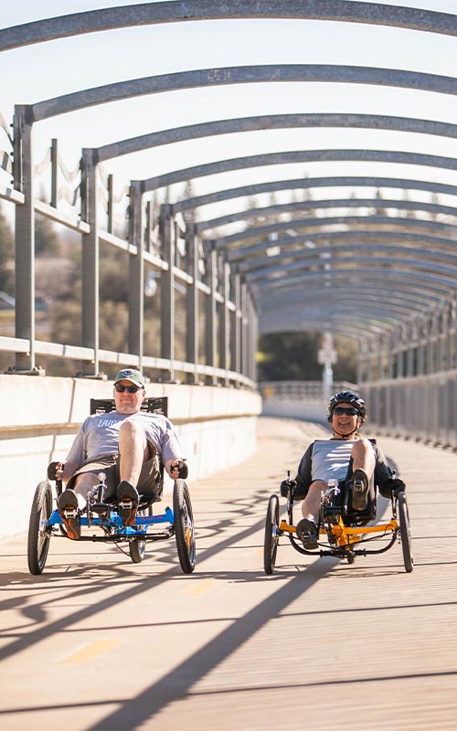 Two ecstatic men riding recumbent trikes over the American River