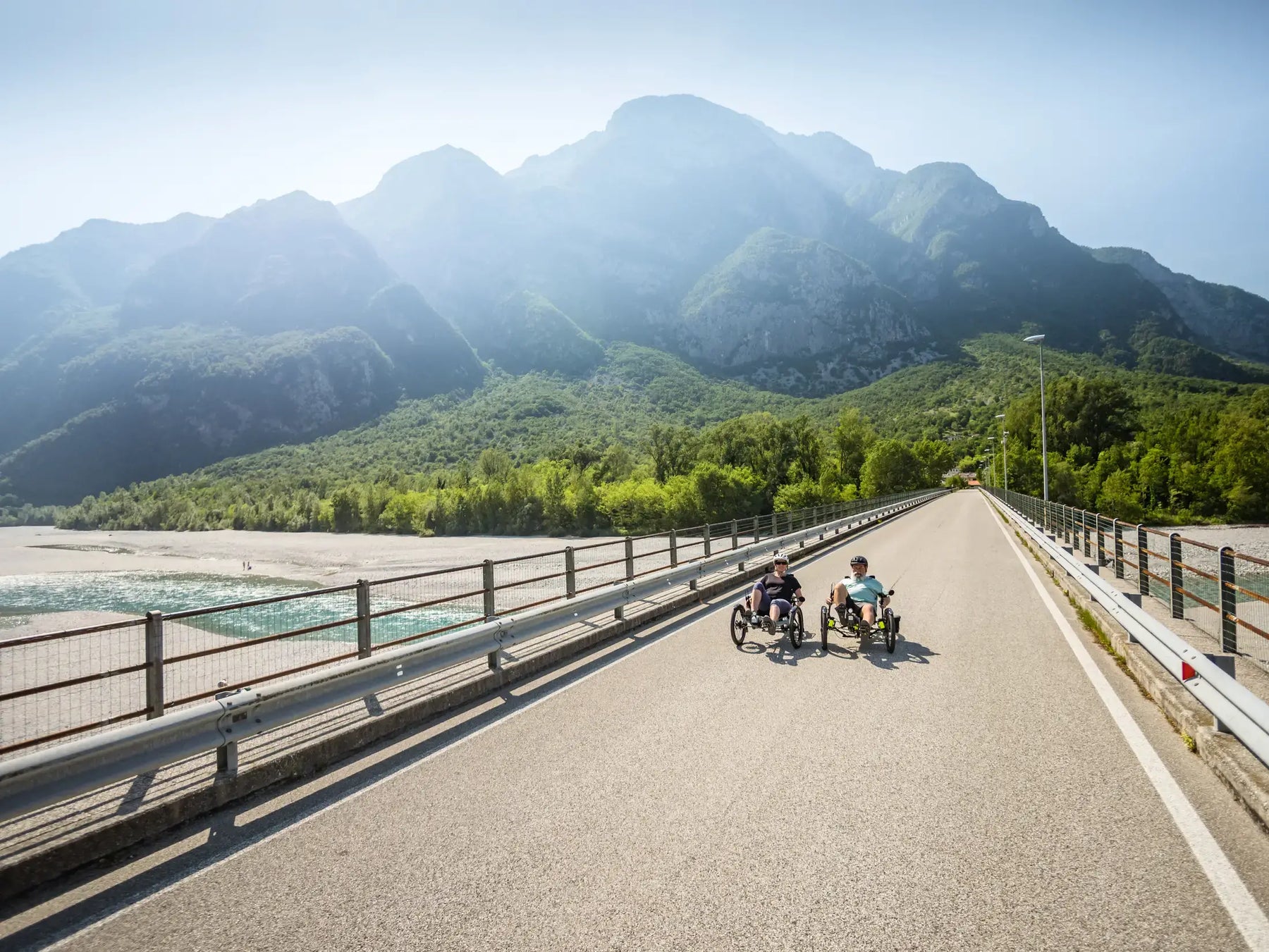 Two riders on AZUB T-Tris 20 recumbent trikes on a mountain river bridge