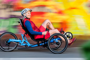 Smiling woman riding a blue AZUB TRIcon 20 folding recumbent trike past a colorful mural