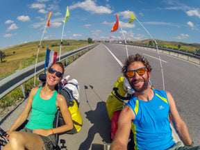 Couple riding loaded AZUB TRIcon 20 recumbent trikes on an open road with flags
