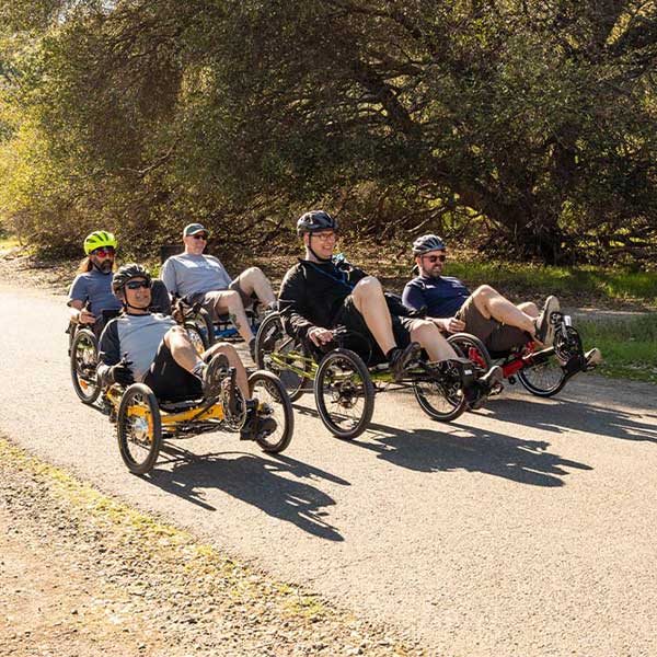 5 members of Laid Back cycles riding recumbent trikes in a formation along Lake Natoma