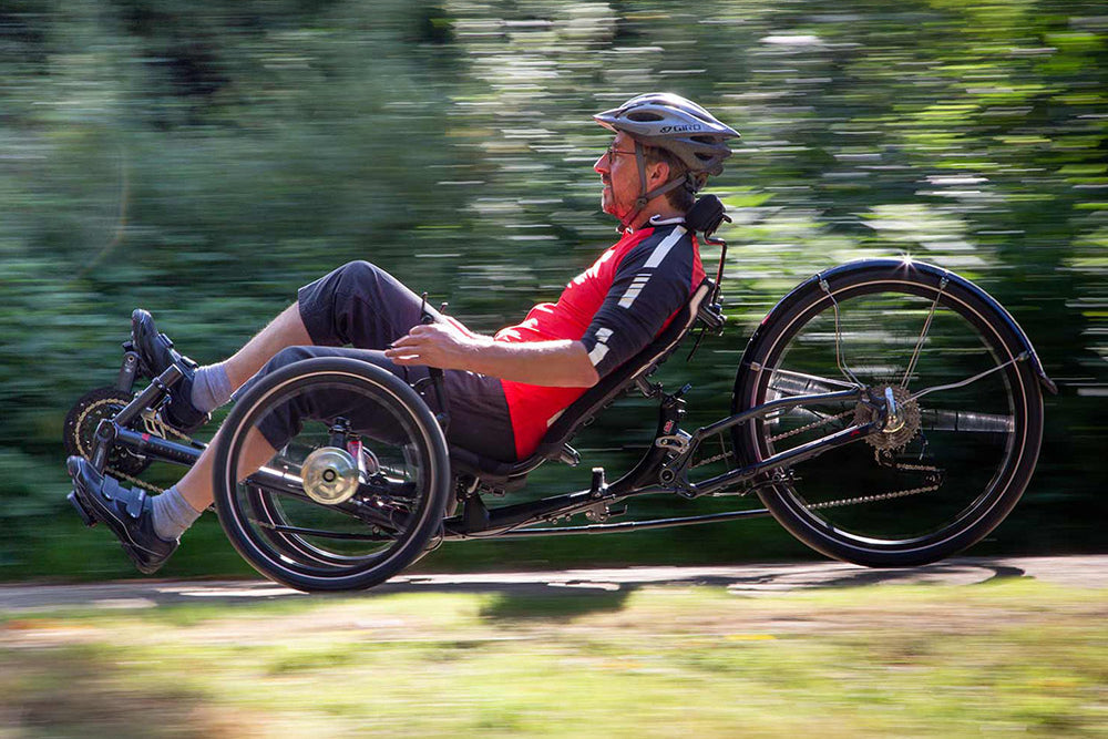 Man riding an ICE Sprint X Tour recumbent trike along a tree-lined path