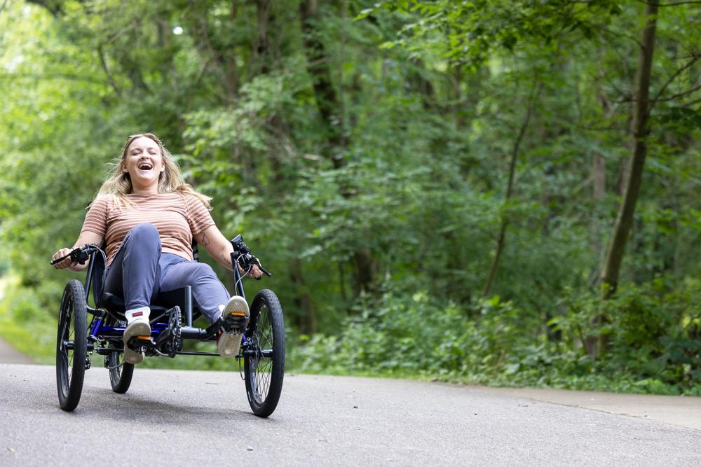 Woman riding a TerraTrike Charge electric recumbent trike on a paved park path