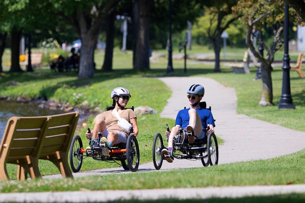 Two riders on GreenSpeed GT20 recumbent trikes on a lakeside park path