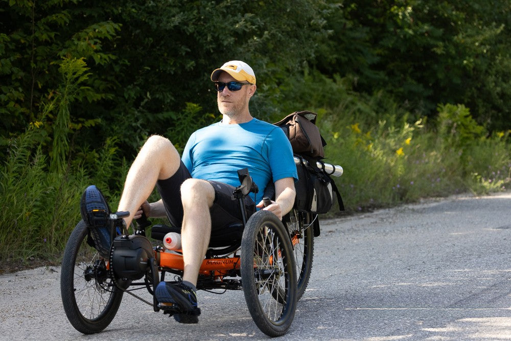 Man riding an orange GreenSpeed Magnum Big Wheel recumbent trike on a country road