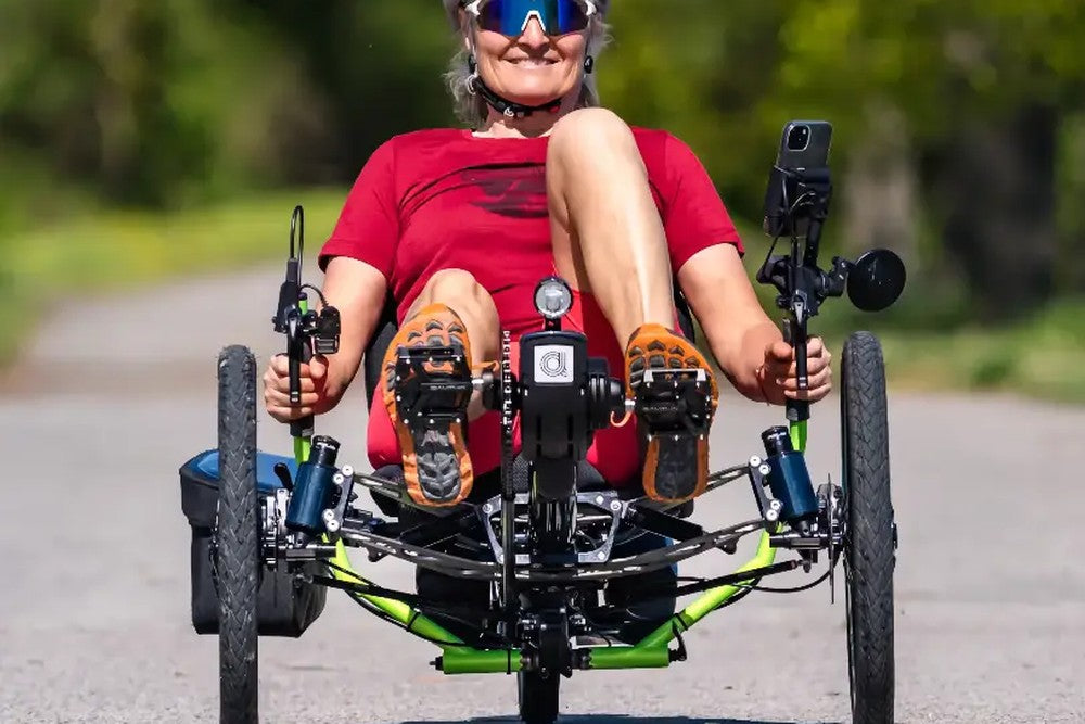 Woman riding a green AZUB Ti-FLY 20 recumbent trike on a paved path