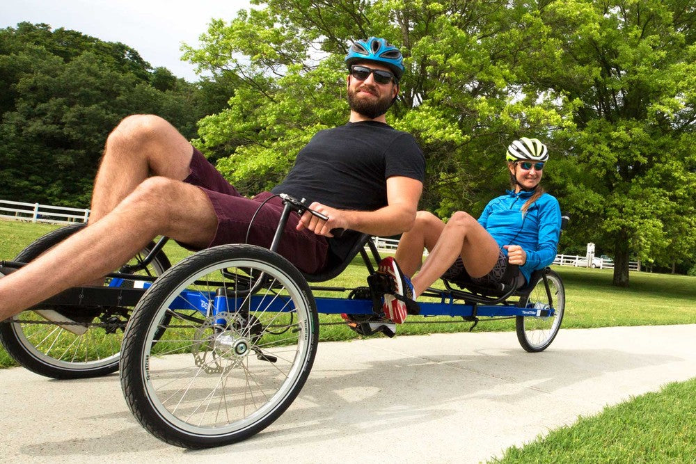 Two riders pedaling a TerraTrike Rover Tandem recumbent tandem trike on a paved park path