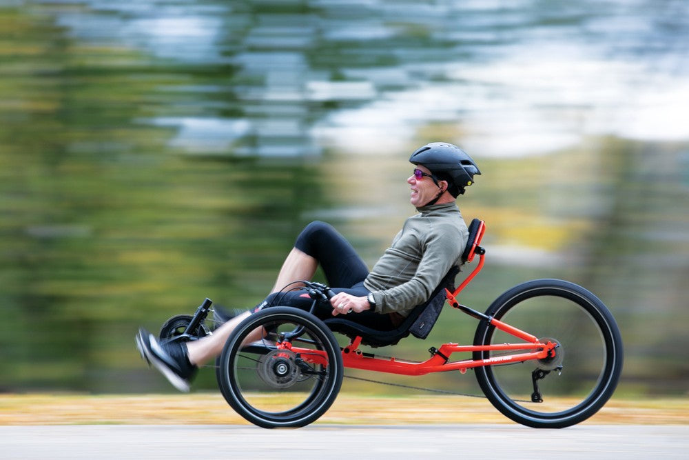 Rider leaning back on a TerraTrike GTS recumbent trike, riding fast on a paved lakeside path